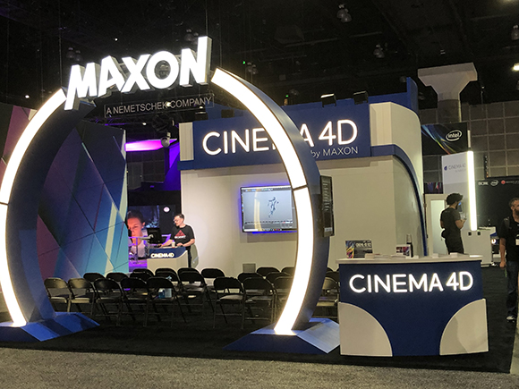 A MAXON Cinema 4D booth with illuminated arches and displays. People are standing at a counter and chairs are set up in front