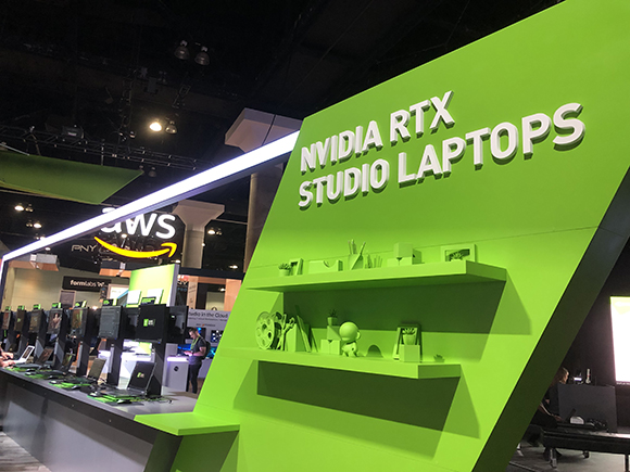 NVIDIA RTX STUDIO LAPTOPS displayed on a bright green structure with shelves holding decorative items. AWS and Amazon logos a