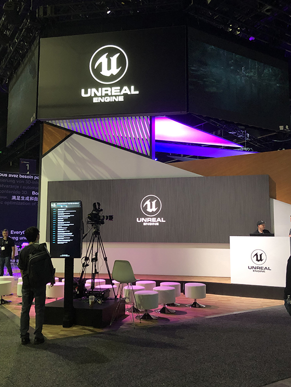 Unreal Engine logo displayed on large screens above a booth with seating and a camera setup.