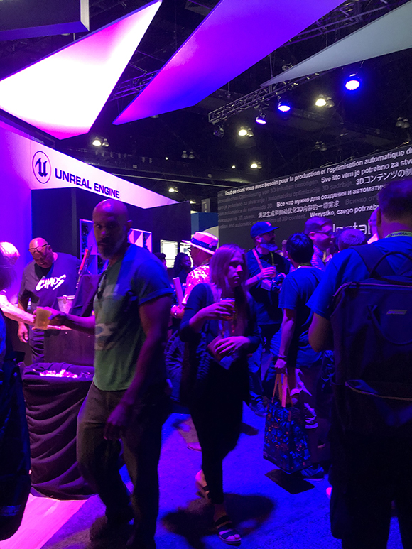 A crowd of people are gathered at a booth with the Unreal Engine logo, under purple and pink lighting.