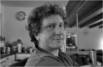 Black and white portrait of a person with curly hair looking toward the camera in an indoor setting.