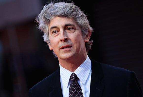 A man with wavy gray hair wearing a white striped shirt and a dark suit jacket.