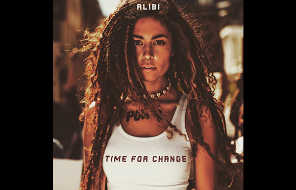 A woman with long dreadlocks wearing a white tank top that reads 'TIME FOR CHANGE'.