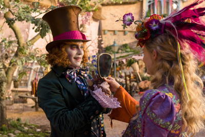 A man in a tall brown top hat holds a small mirror toward a woman with a colorful feathered headpiece.