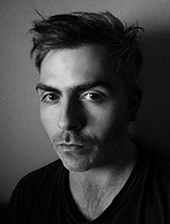 Black and white close-up portrait of a man with short, messy hair looking directly at the camera.