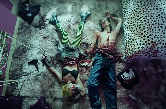 Two bloodied figures lie on a rug amidst scattered clothing and a hair dryer.