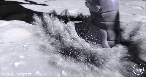 A dark boot steps into grey, powdery lunar soil, causing a spray of dust to kick up.