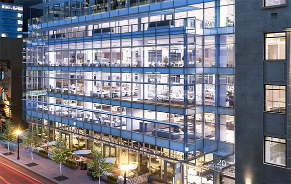 A large glass-walled office building illuminated from within at night, showing multiple floors of workspaces.