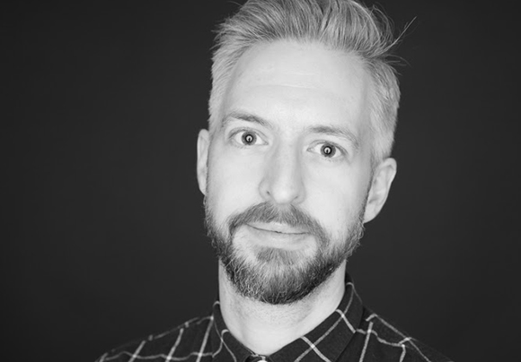 Black and white headshot of a man with light hair and a groomed beard looking toward the camera.