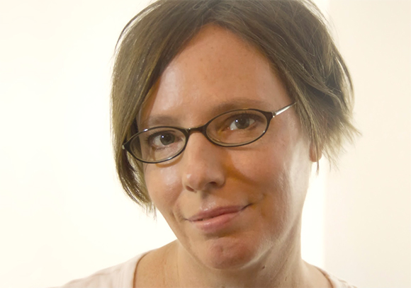 A woman with short brown hair and oval-shaped glasses looking toward the camera.