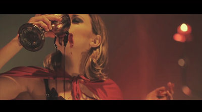 A woman in a red garment drinks a dark red liquid from a silver goblet, with the liquid dripping down her chin.