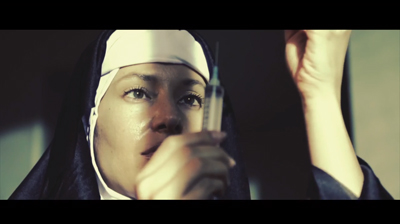 A person wearing a nun's habit holds a medical syringe up to their face.