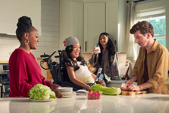Four friends smile and prepare food together in a bright, modern kitchen.