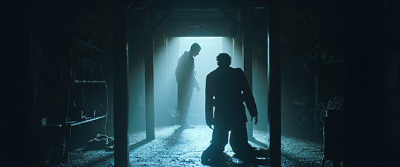 Silhouettes of two people in a dark, smoky room illuminated by a bright doorway.