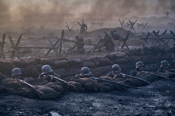 Soldiers in helmets aim rifles from a muddy trench lined with sandbags under a smoky sky.