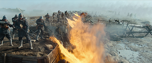 Soldiers in helmets advance through a smoky, muddy battlefield past a large burst of fire.