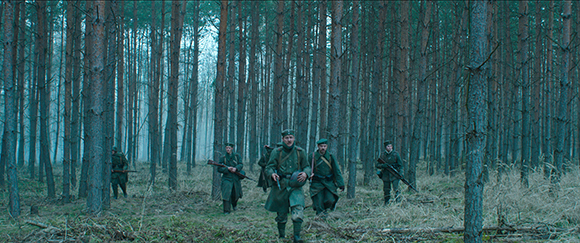 A group of soldiers in military uniforms walking through a misty, dense pine forest.