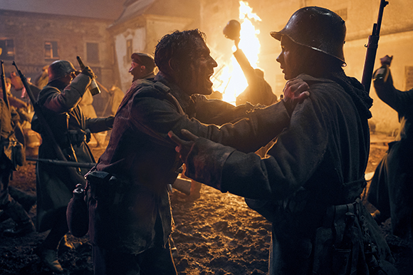 Two soldiers in military uniforms grapple closely amidst a chaotic, firelit nighttime battlefield.