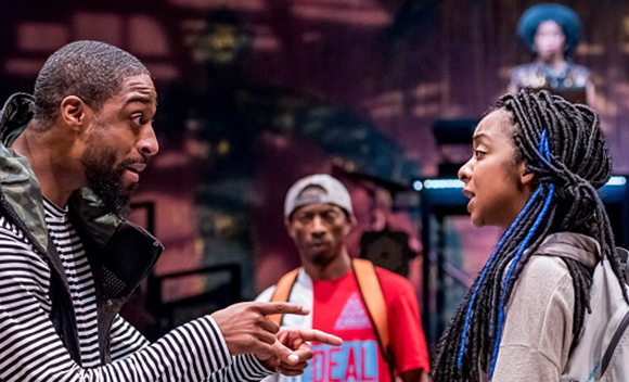 A man in a striped shirt gestures toward a woman with braided hair during a conversation.