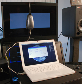 A white laptop displaying a globe, a large monitor, a headset, and a studio monitor speaker.
