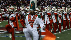 Marching band members in white and orange uniforms performing on a green field.