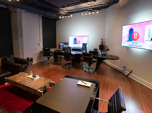 A modern office interior with wooden floors, dark desks, and large computer monitors.