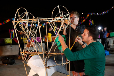 Two men work together to build a large, circular wooden frame structure outdoors at night.