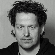 Black and white headshot of a man with wavy hair looking directly at the camera.