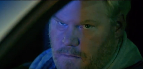 Close-up of a bearded man's face illuminated by blue and green light in a dark setting.