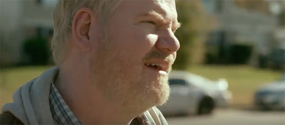 A fair-skinned man with blonde hair and a beard smiles while looking to the side outdoors.