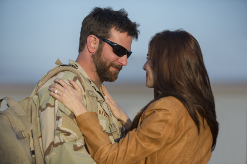 A man in camouflage and sunglasses embraces a woman in a brown leather jacket.