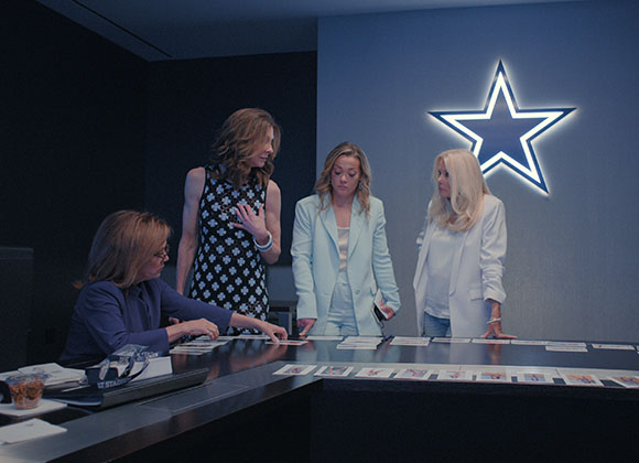 Four women stand around a dark conference table in a room featuring a large glowing blue and white star logo.