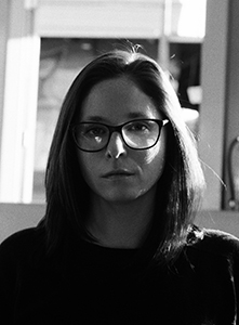 Black and white portrait of a woman with long hair and glasses looking directly at the camera.