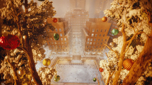 View of city buildings through snow-covered trees decorated with colorful Christmas ornaments.