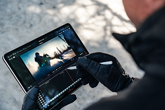 A person in black gloves uses a stylus to edit a video of a snowy landscape on a tablet.
