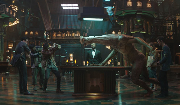 A large, pale creature lunges across a table toward several men in a dark, upscale room.