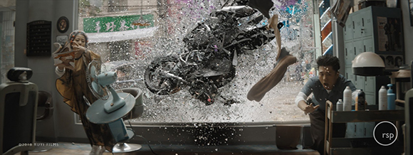 A black motorcycle smashes through a glass storefront window, sending shards flying toward people inside.
