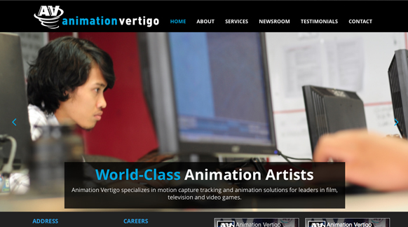 A young man works at a computer desk in a studio setting with multiple monitors.