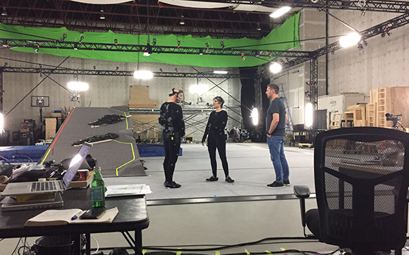 Three people stand in a large film studio with a green screen and production equipment.
