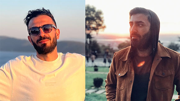 Two men posing outdoors; one in a white t-shirt and sunglasses, the other in a brown jacket.