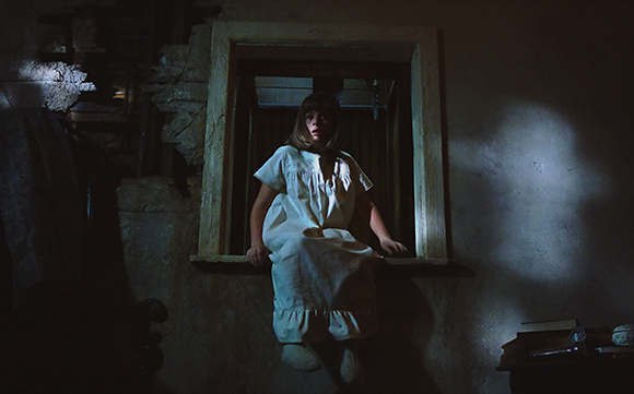 A young girl in a white dress sits in a dark, rustic window frame.