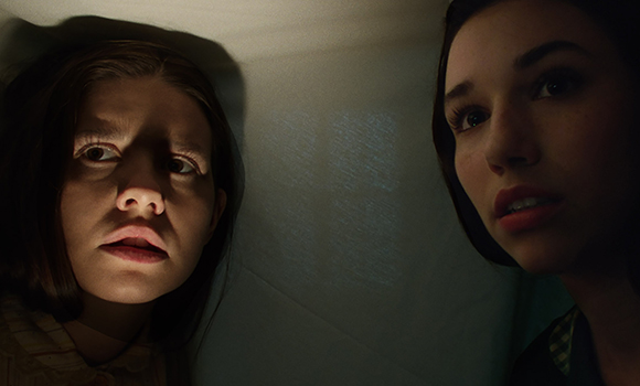 Two young women peer into a dark space with worried expressions.
