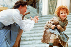 A woman in a white blouse leans toward a young girl with curly red hair in a patterned dress.