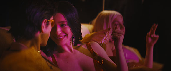 A smiling woman with dark hair leans toward a man in a warm, low-light indoor setting.