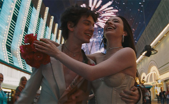 A smiling young man and woman embrace outdoors at night with fireworks in the background.