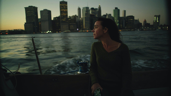 A woman gazes at a lit city skyline from a moving boat during twilight.
