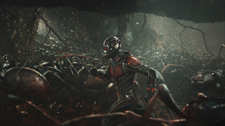 A person in a black and red armored suit crouches amidst a swarm of large, dark ants in a dark, cavernous setting.