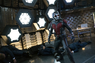 A person in a red and silver superhero suit stands in a futuristic room with hexagonal lights and fallen people.