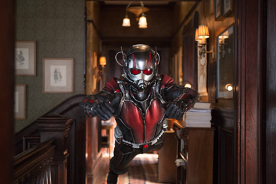 A person in a red and black superhero suit with a silver helmet flies toward the camera in a dimly lit hallway.