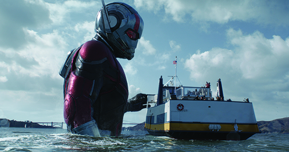 A giant person in a red and silver armored suit looms over a small white ferry boat on the ocean.